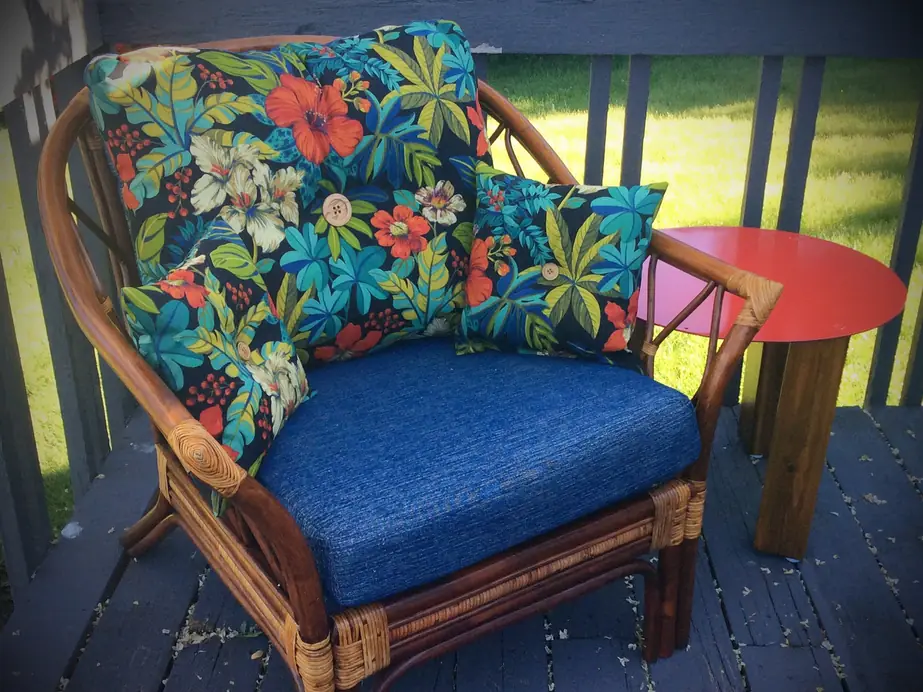 Rattan armchair with a navy seat cushion and tropical-print back pillows on a deck