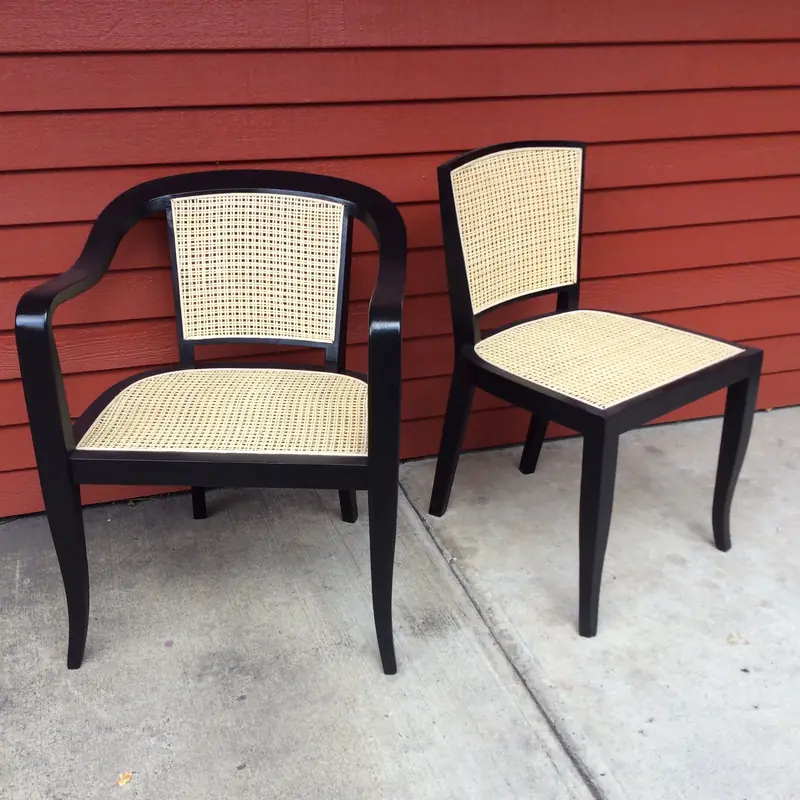 Two black chairs with new pressed-cane seats and backs against red siding