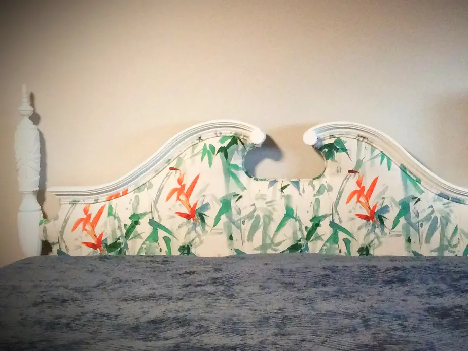 Shaped vintage headboard re-covered in a white print of green bamboo leaves and orange flowers